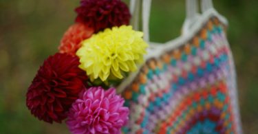 Colorful handmade crochet market bag holding a bouquet of flowers