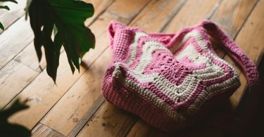 Pink and white handmade crochet tote bag on a wooden floor