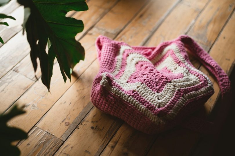Pink and white handmade crochet tote bag on a wooden floor